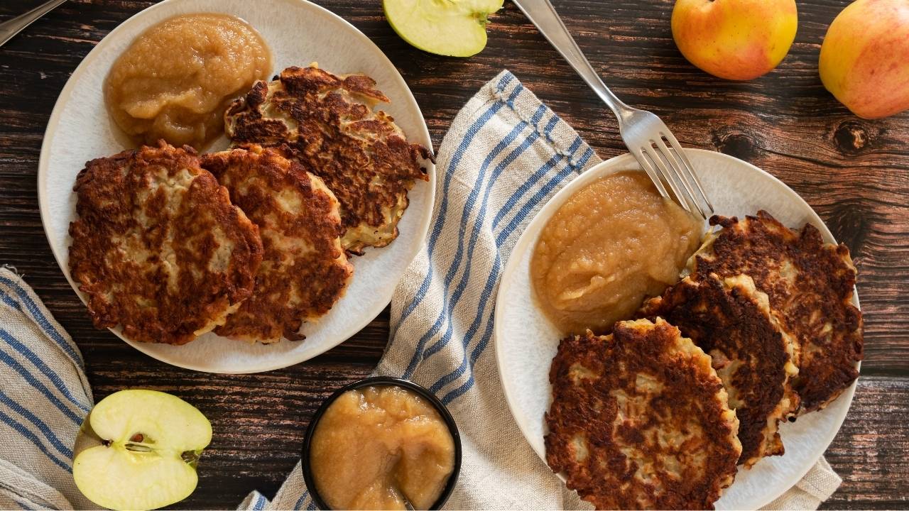 Fried golden crisp potato pancakes served with apple sauce on plates.