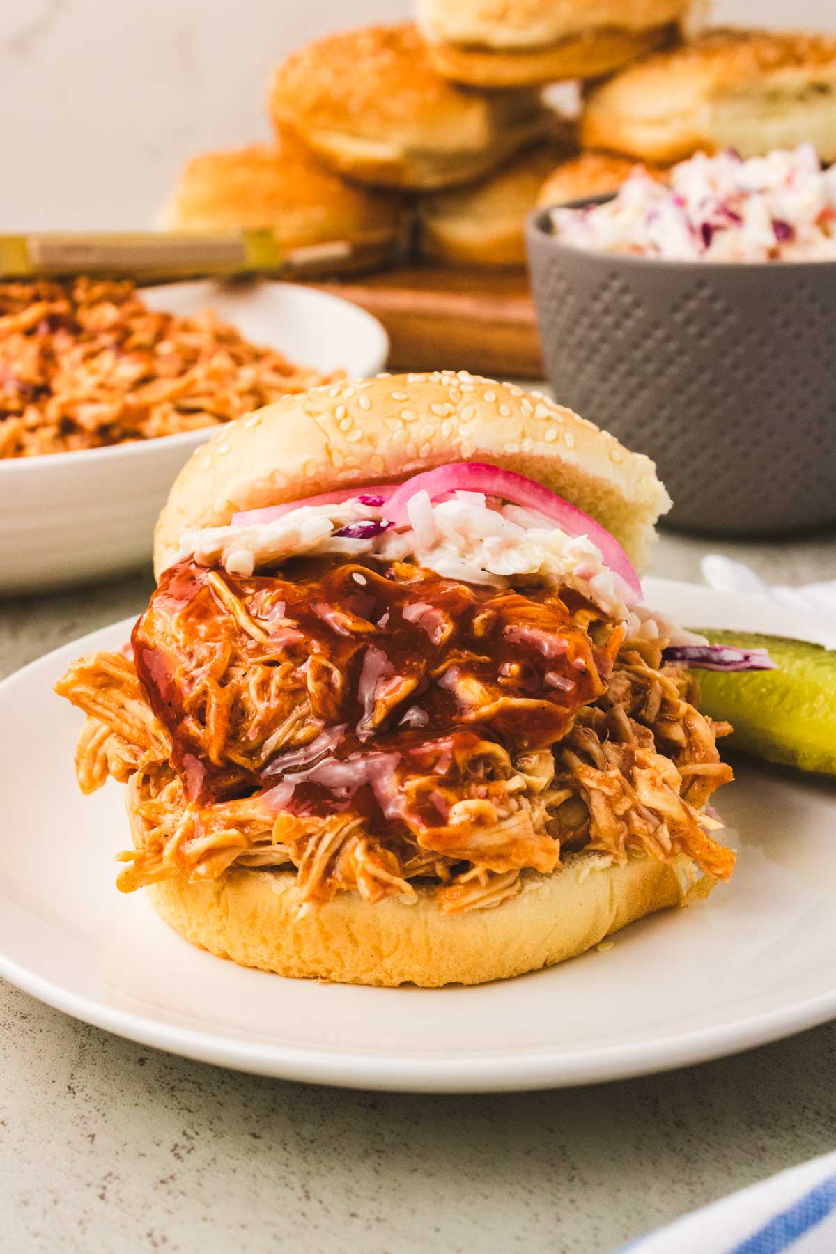 Slow cooked BBQ shredded chicken breasts piled on top of a bun with cole slaw and BBQ sauce.