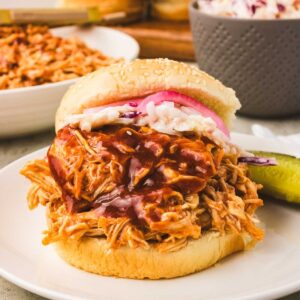 Slow cooked BBQ shredded chicken breasts piled on top of a bun with cole slaw and BBQ sauce.