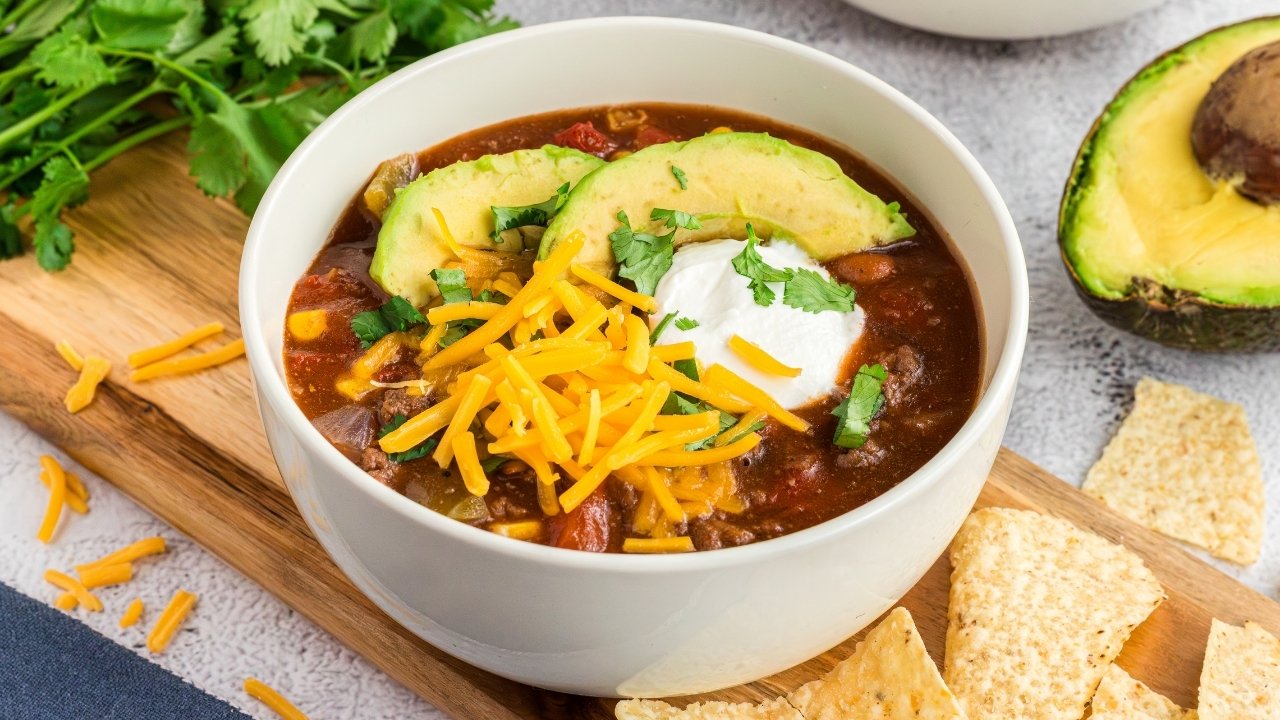 A bowl of hearty chili topped with shredded cheese, avocado, and sour cream.
