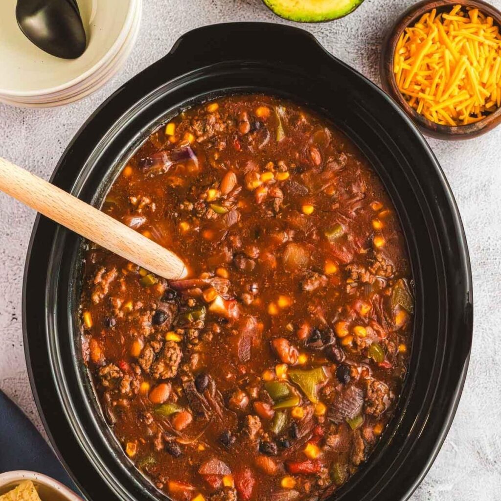 A Crock Pot slow cooker full of meaty chili with vegetables and beans.
