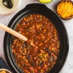 A Crock Pot slow cooker full of meaty chili with vegetables and beans.