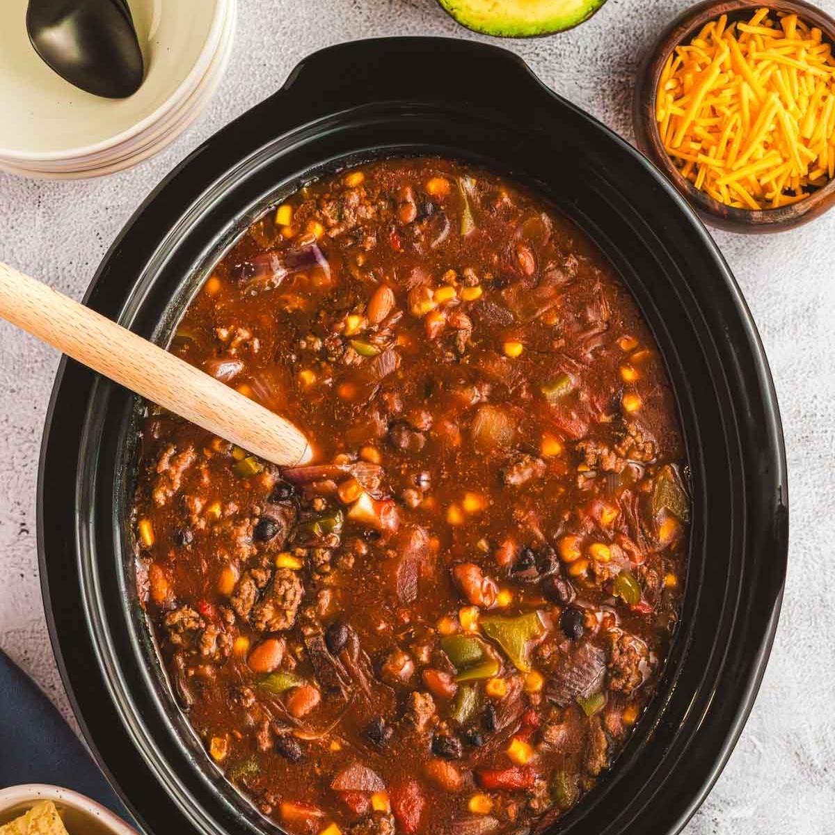 A Crock Pot slow cooker full of meaty chili with vegetables and beans.