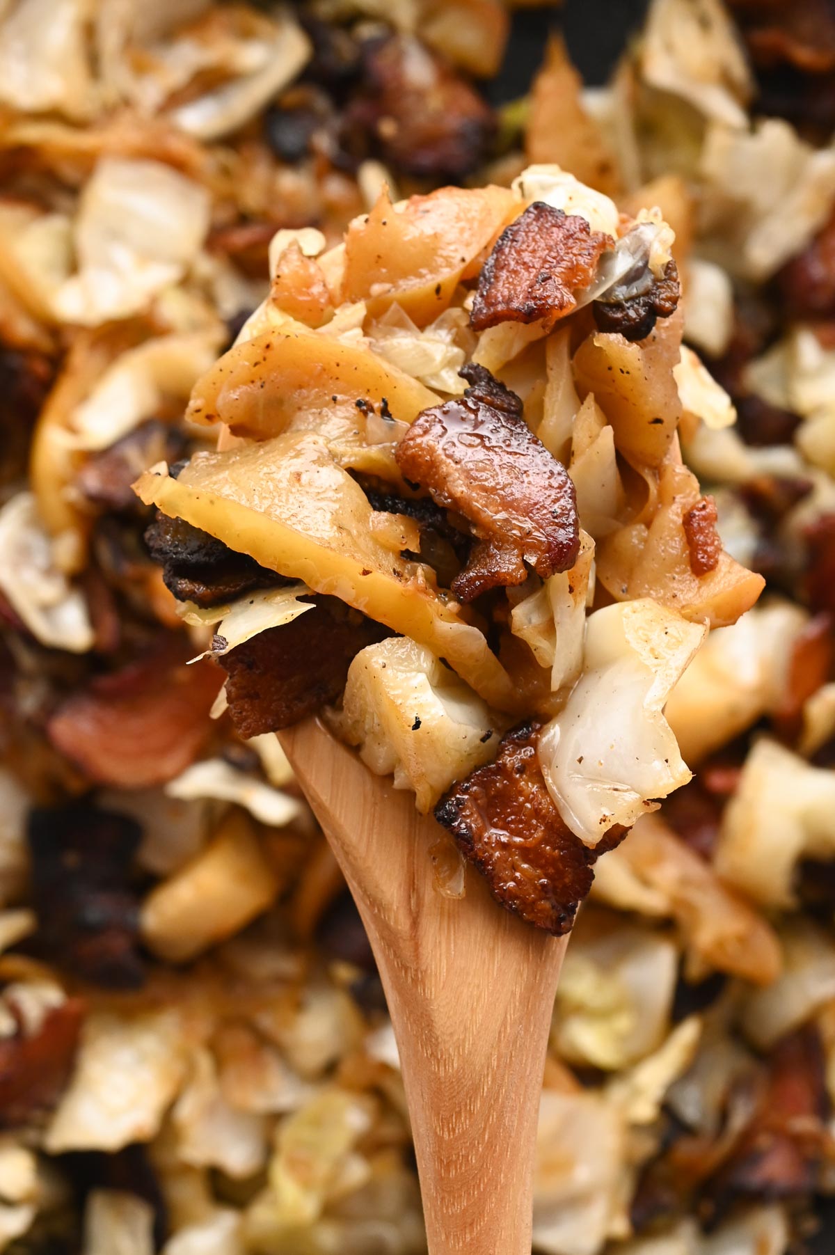 A wooden spoon full of fried cabbage and bacon.