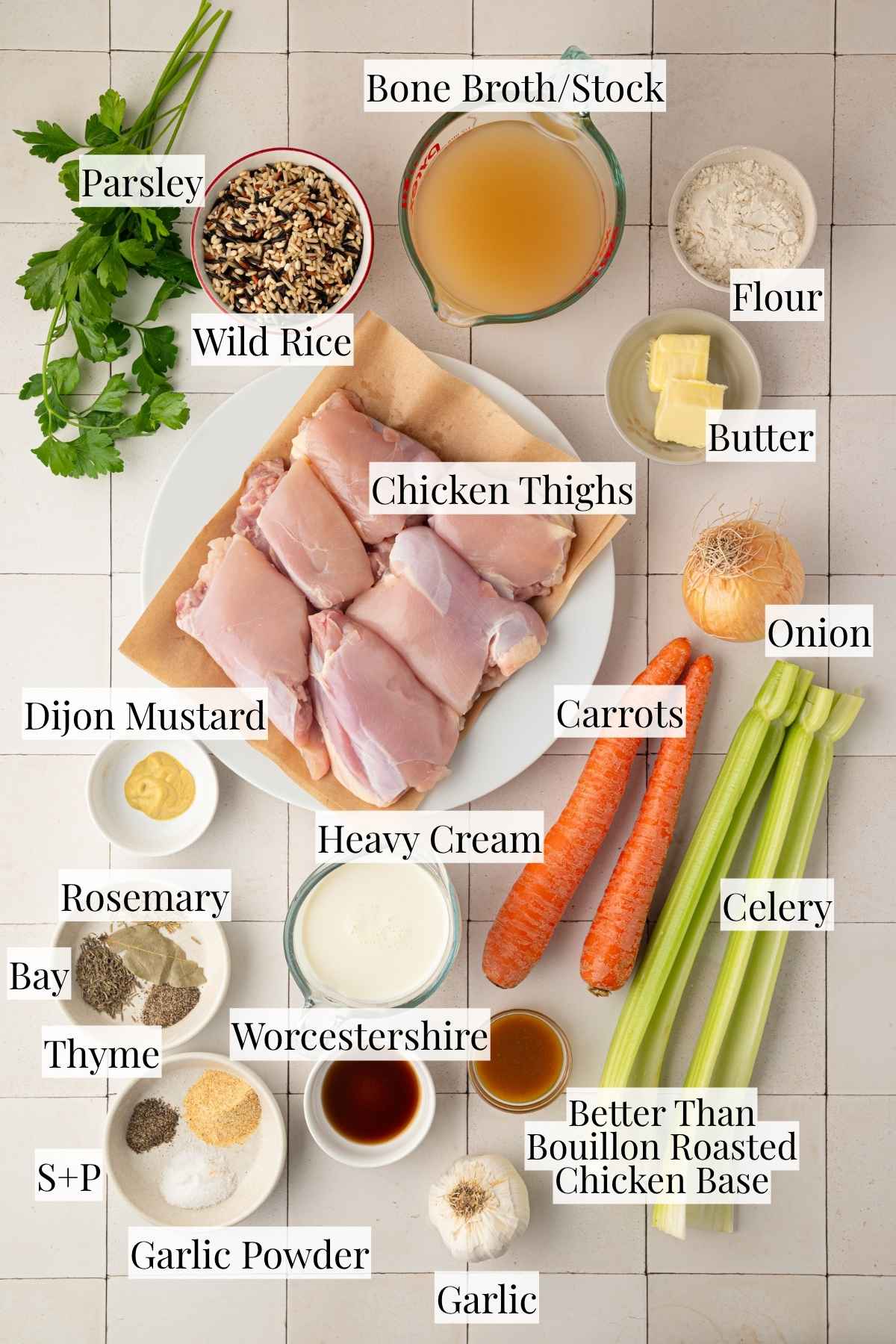 Ingredients for creamy chicken and wild rice soup arranged together, including chicken thighs, wild rice blend, carrots, celery, onion, garlic, chicken broth, heavy cream, butter, flour, herbs, and seasonings.