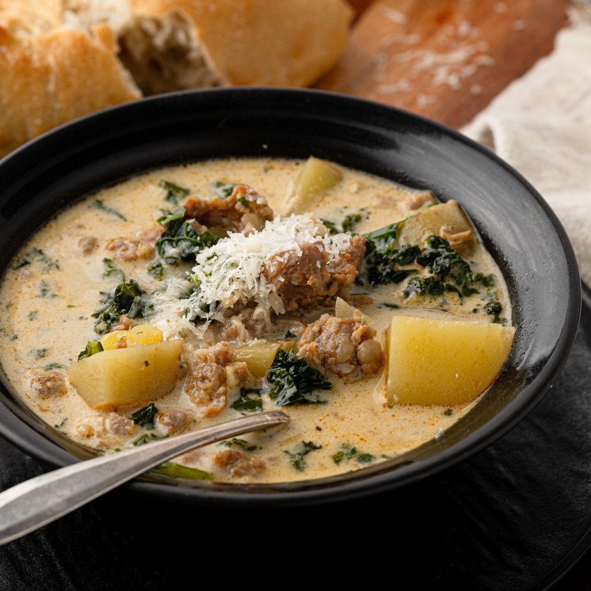 A bowl of sausage, potato and kale soup with Italian sausage, chunks of potatoes, and fresh kale in a creamy Parmesan broth, topped with freshly grated Parmigiano Reggiano.