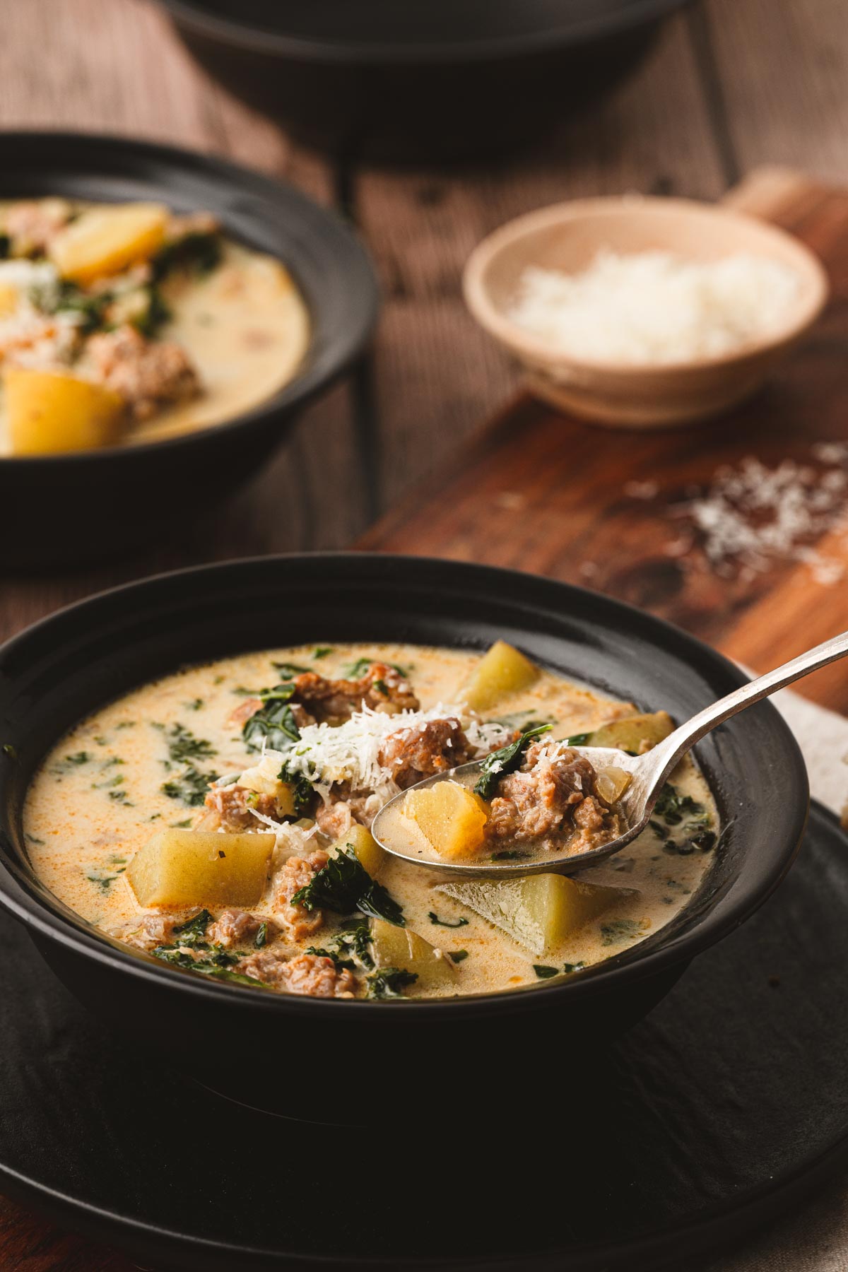 A bowl of sausage, potato and kale soup with Italian sausage, chunks of potatoes, and fresh kale in a creamy Parmesan broth, topped with freshly grated Parmigiano Reggiano.
