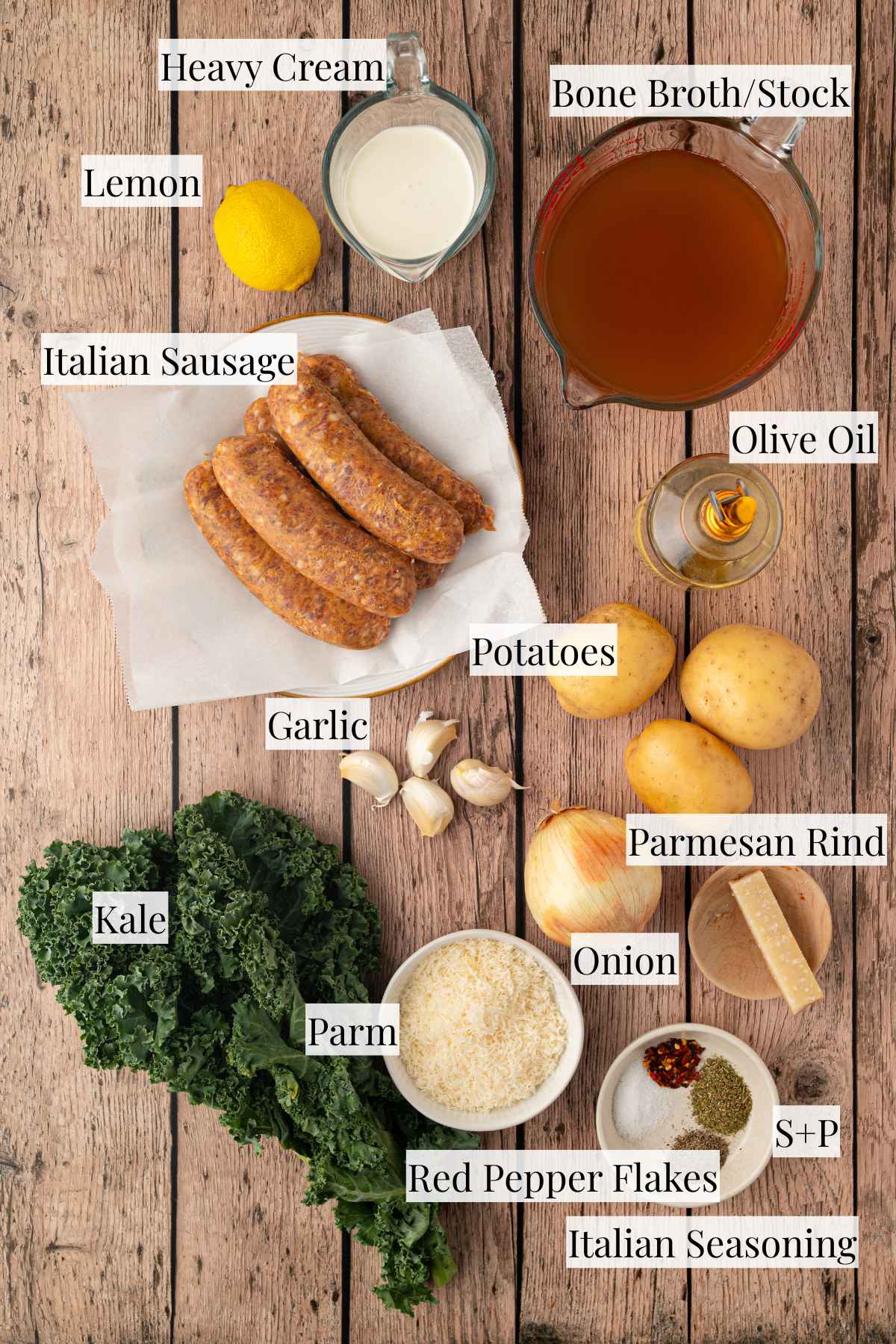 Ingredients for sausage, potato and kale soup arranged together, including Italian sausage, Yukon Gold potatoes, fresh kale, onion, garlic, chicken broth, heavy cream, Parmesan cheese, lemon, and seasonings.