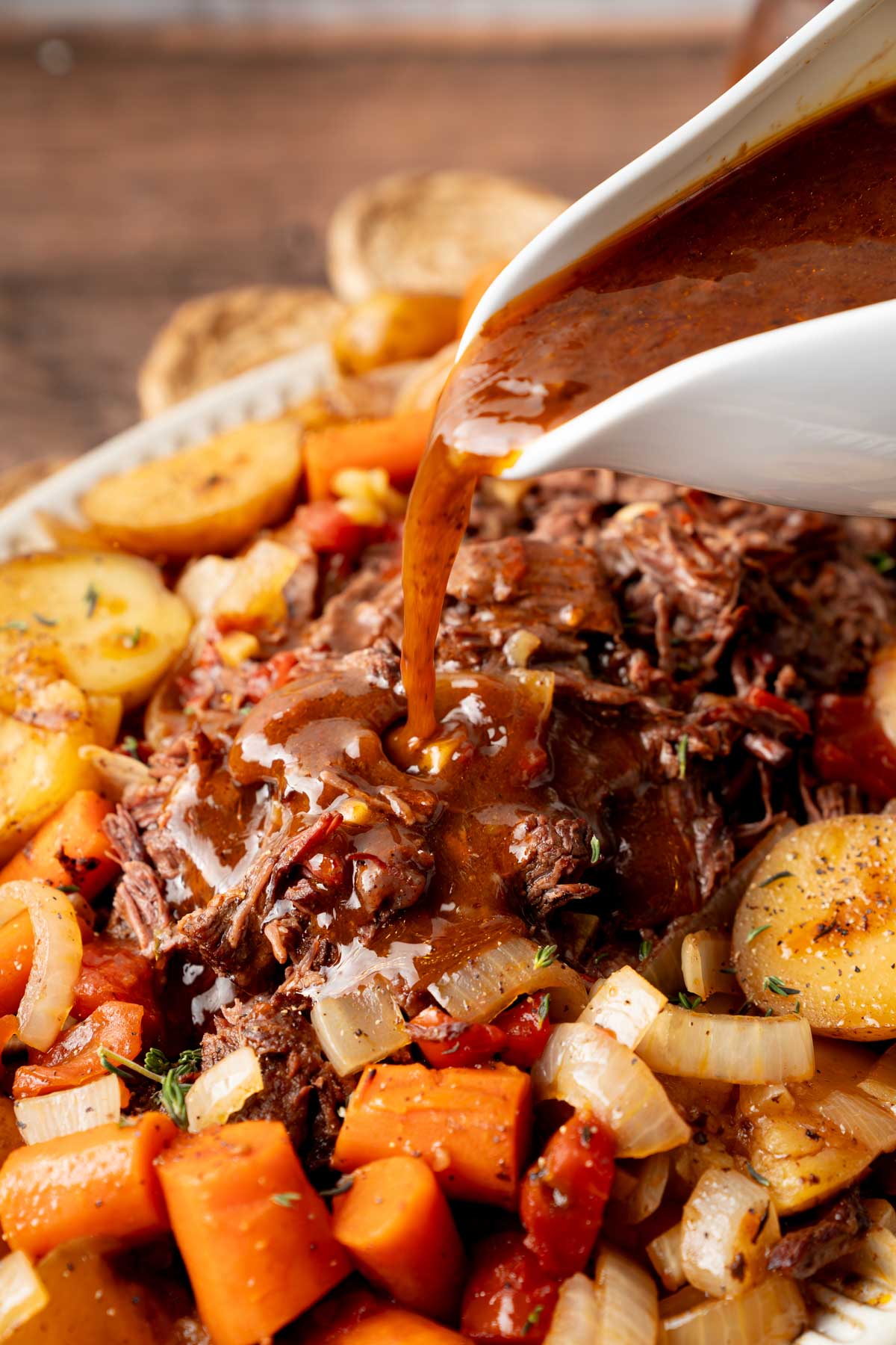 A platter of the slow cooked beef and vegetables ready to serve at the dinner table. Thick homemade gravy is being poured on top.