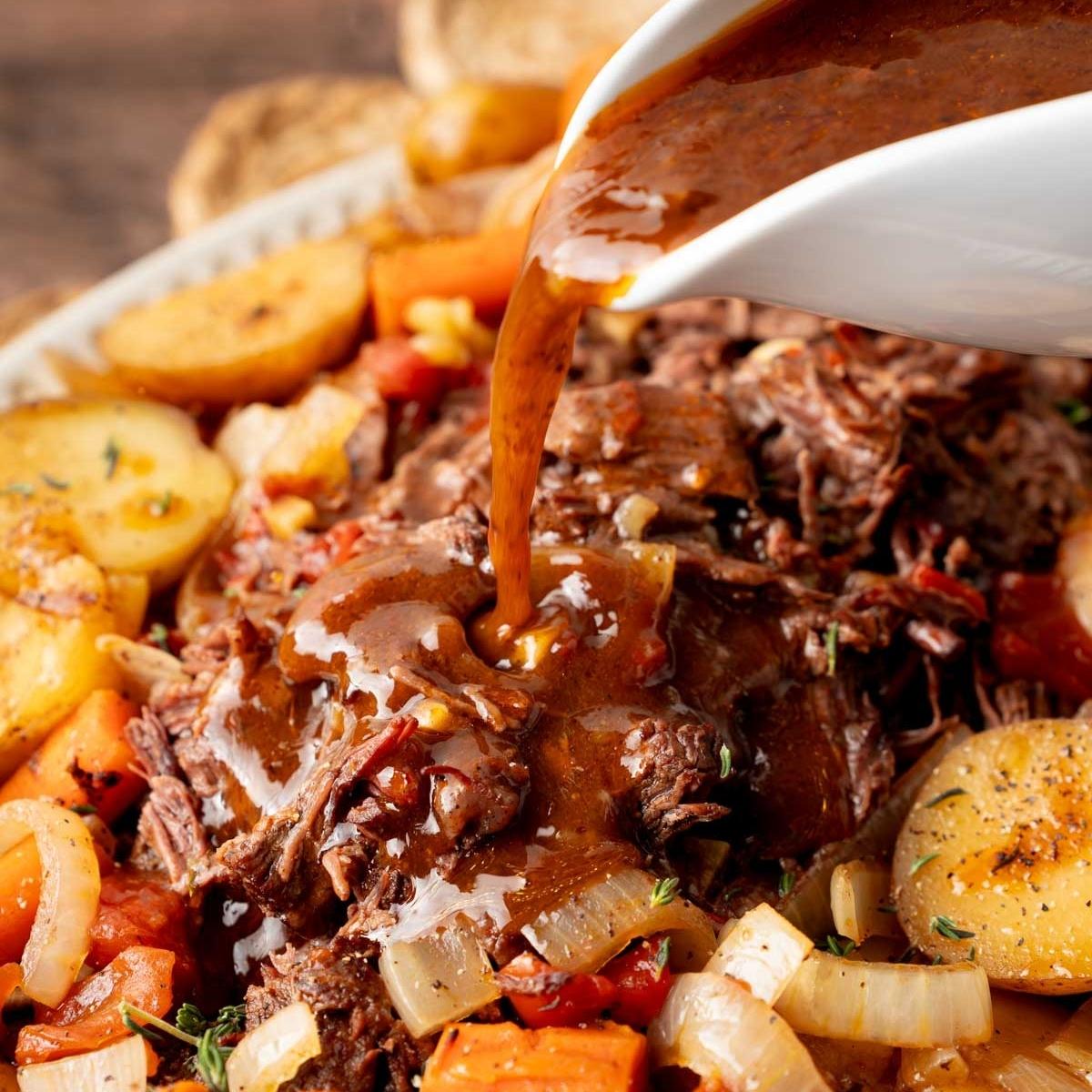 A platter of the slow cooked beef and vegetables ready to serve at the dinner table. Thick homemade gravy is being poured on top.