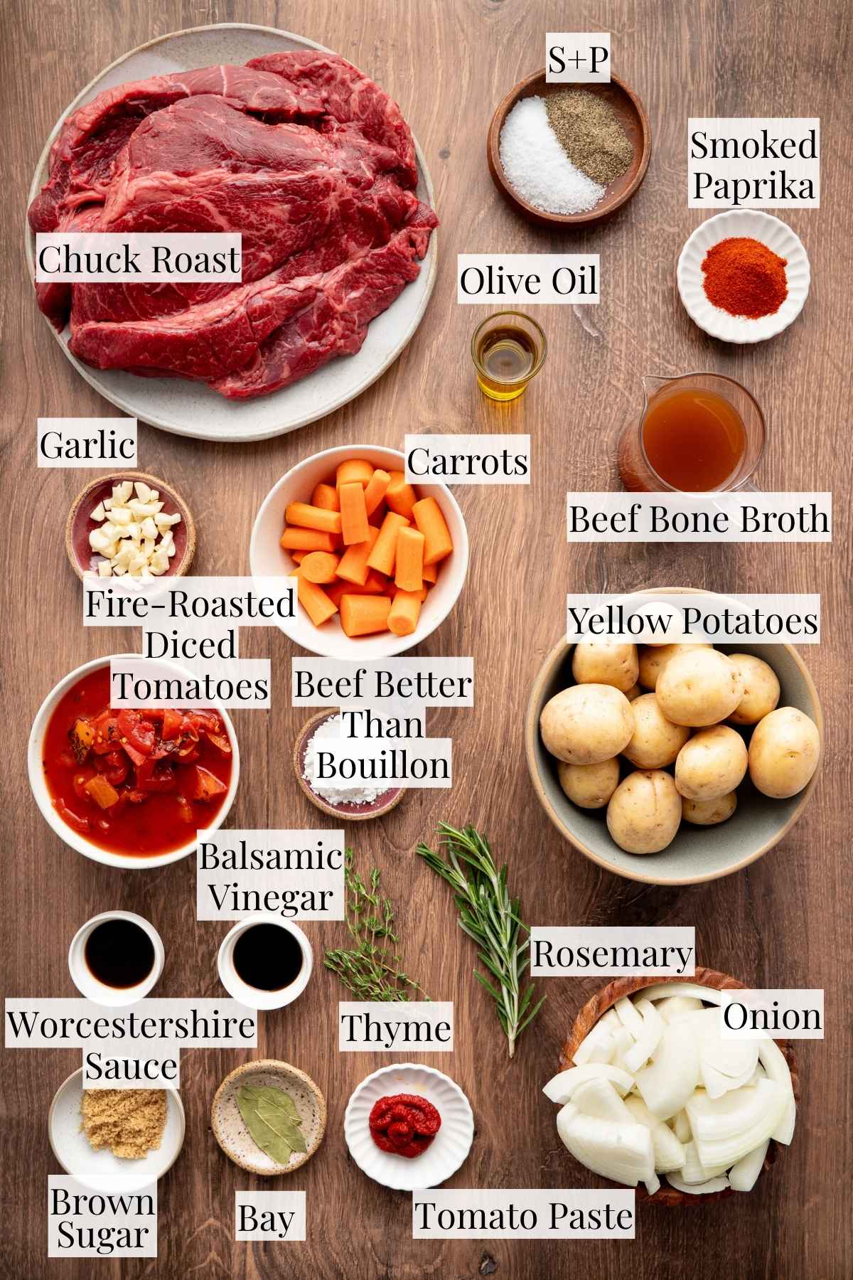 Ingredients for slow cooker beef roast arranged together, including chuck roast, baby yellow potatoes, carrots, onion, garlic, tomatoes, beef broth, herbs, and seasonings.